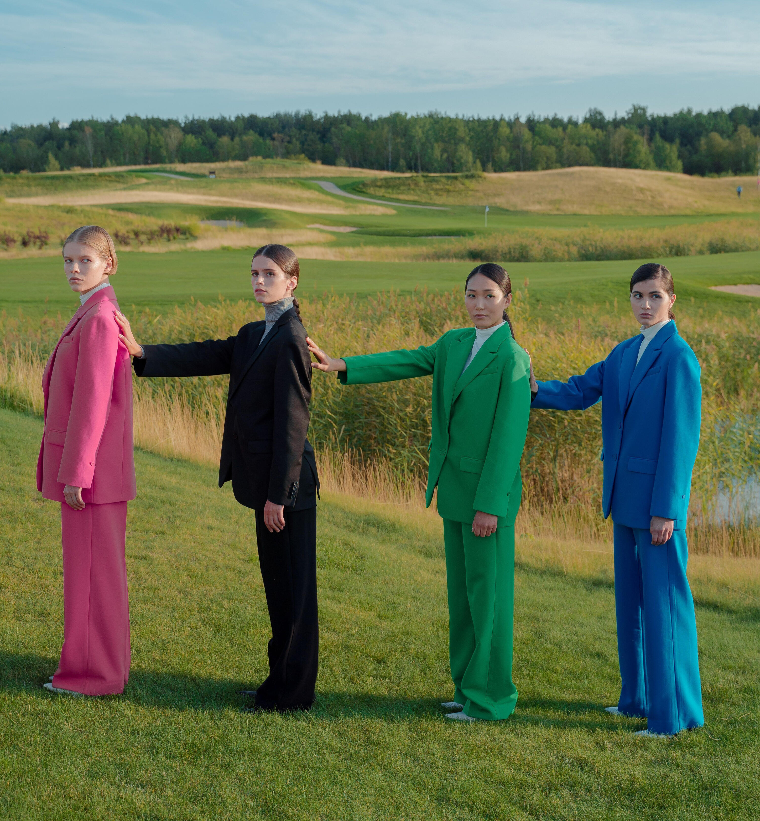 The Expansion Room Image of ladies wearing different colored suits and right hands stretched at the back of the person in front